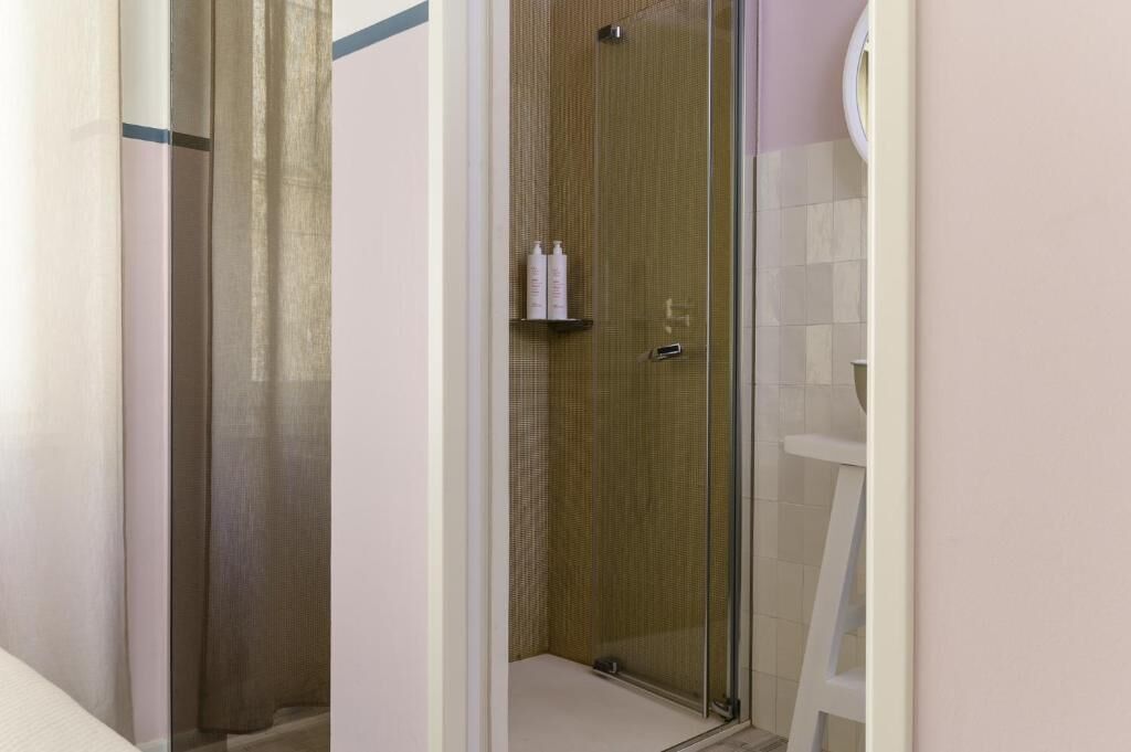 A glass-enclosed shower area with a wooden door, a white towel rack, and a white chair.
