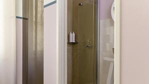 A glass-enclosed shower area with a wooden door, a white towel rack, and a white chair.