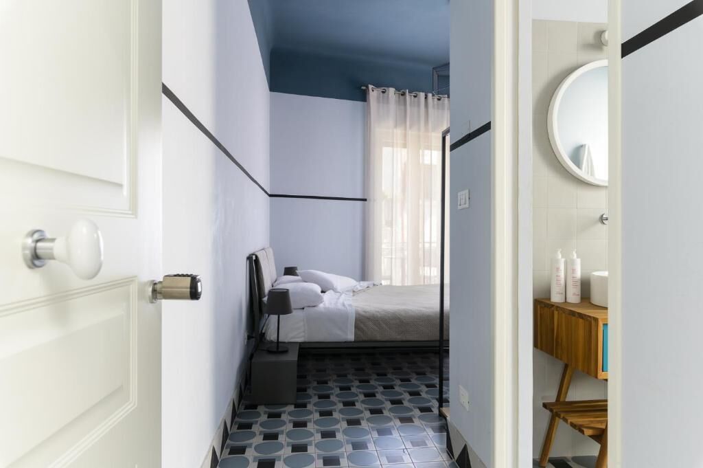 A bedroom with a bed, a bedside table, a mirror, and a bathroom with a toilet and sink.