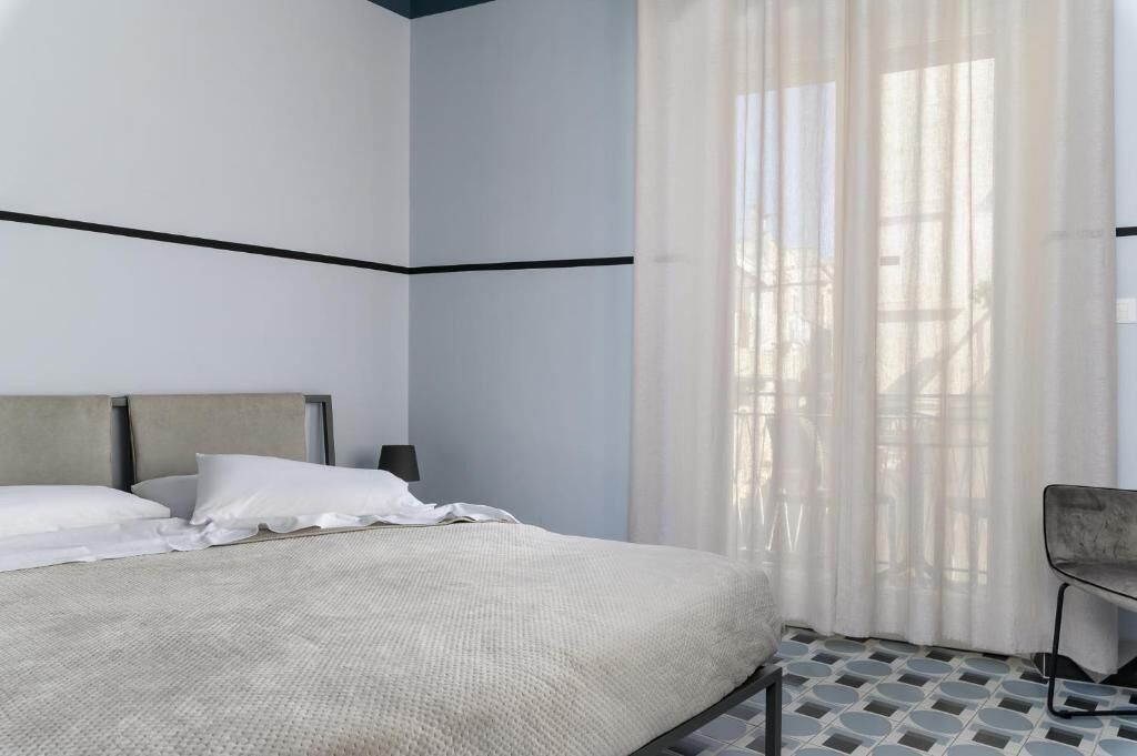 A bedroom with a bed, a chair, and a window with sheer curtains.