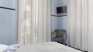 Ein Hotelzimmer mit Bett, einem Sessel, einem an der Wand befestigten Fernseher und durchscheinenden Vorhängen.