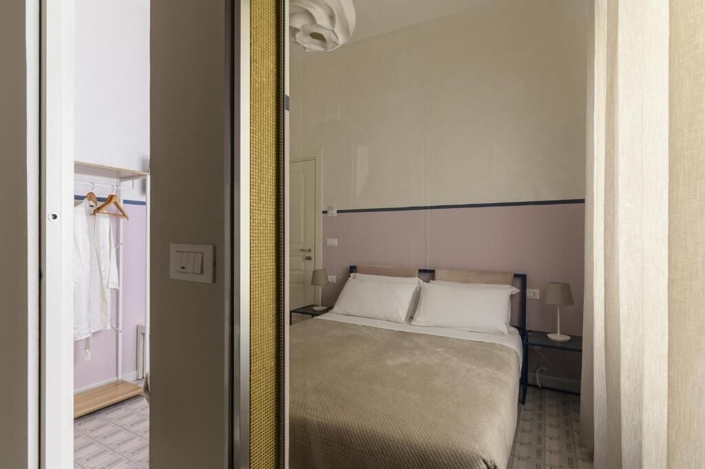 Hotellihuone, jossa on sänky, yöpöydät, vaatekaappi ja peili.