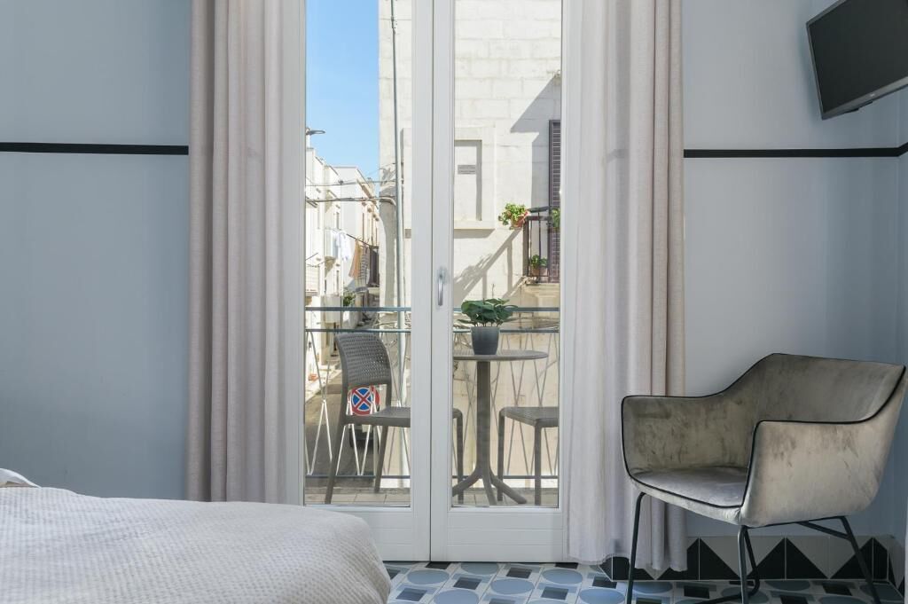 A hotel room with a bed, a chair, a balcony with a table and chairs, and a TV mounted on the wall.