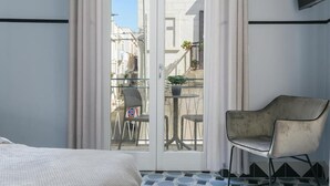 A hotel room with a bed, a chair, a balcony with a table and chairs, and a TV mounted on the wall.