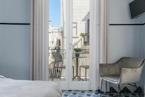 A hotel room with a bed, a chair, a balcony with a table and chairs, and a TV mounted on the wall. - Unico Art Decor (Ostuni)
