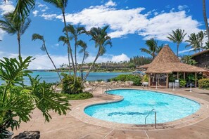 Ein Swimmingpool mit einer strohgedeckten Struktur, umgeben von Palmen und Blick auf den Ozean.
