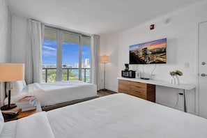 A hotel room with two beds, a TV, a desk, and a window with a city view. - Ocean & Canal View Studio Beach 8 Min Pool Gym 804 (Hallandale Beach)