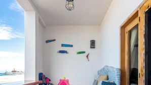 Ein Balkon mit einem Bett, einem Holzstuhl und verschiedenen Strandspielzeugen.