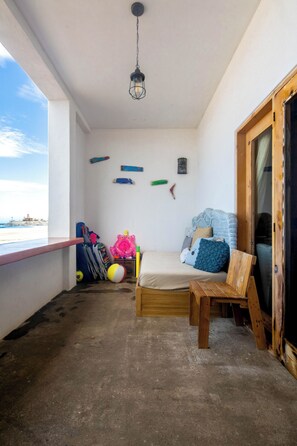 Ein Balkon mit einem Bett, einem Holzstuhl und verschiedenen Strandspielzeugen.