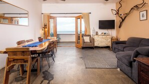 Ein Zimmer mit einem Holzesstisch, Stühlen, einer Couch, einem Fernseher und einem Deckenventilator.