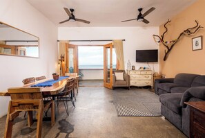 Ein Zimmer mit einem Holzesstisch, Stühlen, einer Couch, einem Fernseher und einem Deckenventilator.