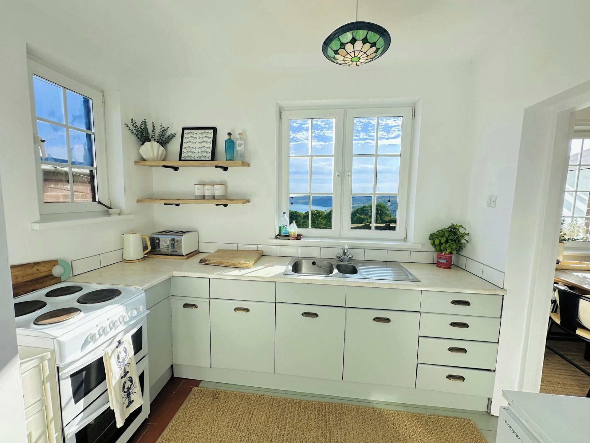 A kitchen with a stove, sink, and window overlooking a scenic view.