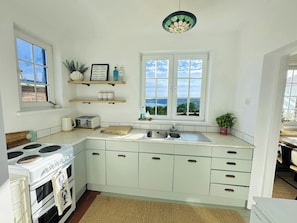 A kitchen with a stove, sink, and window overlooking a scenic view. - 3 Hilltop Way, Aberporth (Aberporth)