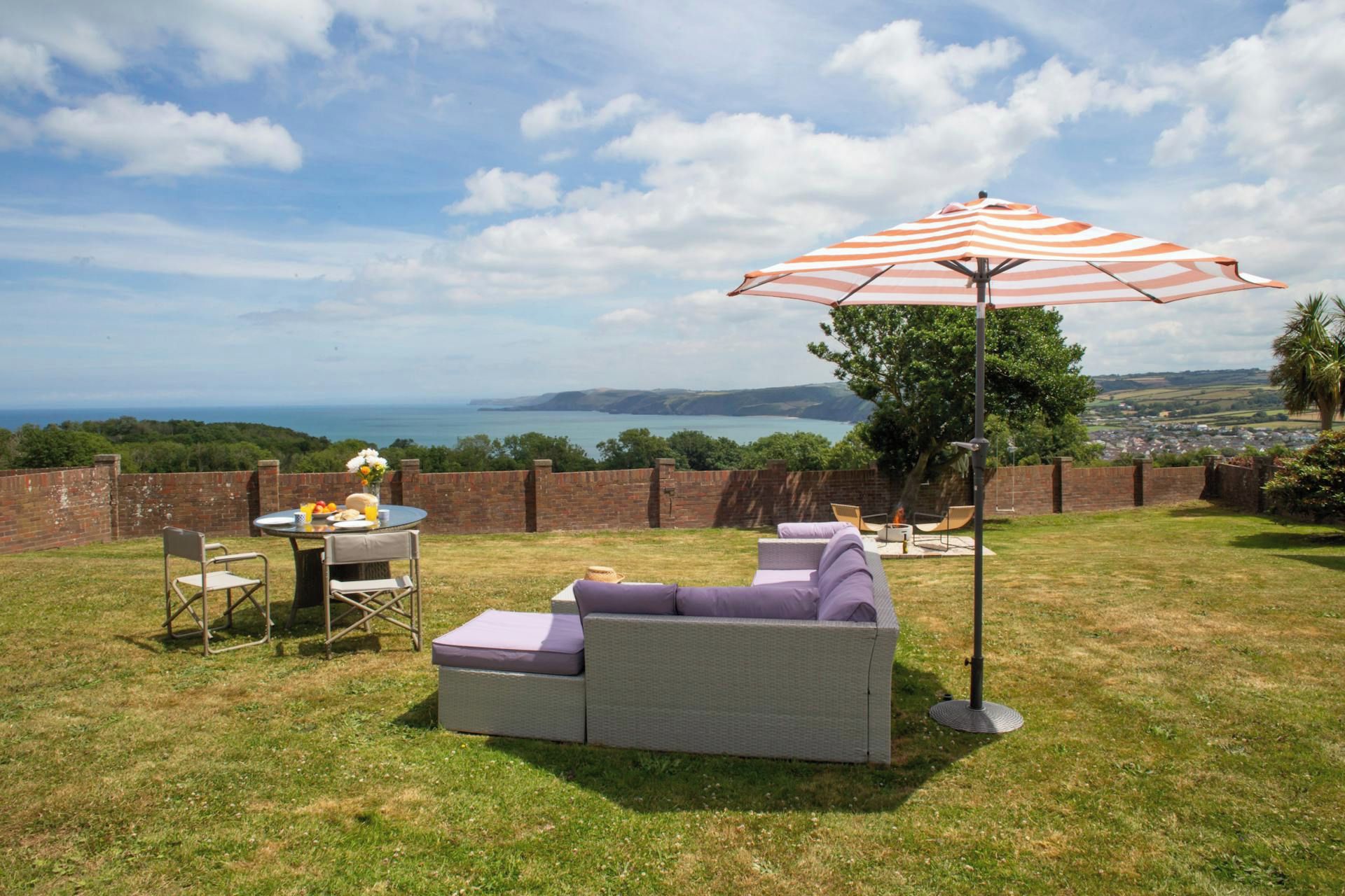 Garden seating area with sofa, umbrella and table set overlooking the sea