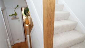 A staircase with carpeted steps, a wooden handrail, and a white door leading to a room with a bed and a plant. - 3 Hilltop Way, Aberporth (Aberporth)