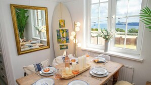 A dining area with a table set for four, a surfboard, and a view of the sea. - 3 Hilltop Way, Aberporth (Aberporth)