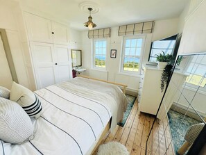 Una camera da letto con un letto, una cassettiera, uno specchio e finestre con vista.