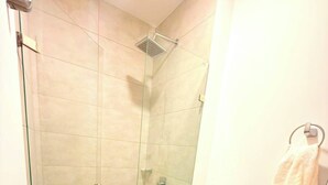 Ein Badezimmer mit einer gläsernen Duschkabine, Toilette und Waschbecken. Ein Handtuch hängt an der Wand.