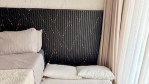Ein Hotelzimmer mit einem Bett, Kissen, einem Kopfteil und einem Fenster mit Vorhängen.