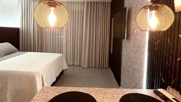 Ein modernes Hotelzimmer mit einem Bett, zwei Pendelleuchten, einem großen Spiegel und einer strukturierten Wand.