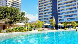 Ein Hotel mit Schwimmbad, mehreren Balkonen und blauem Himmel.