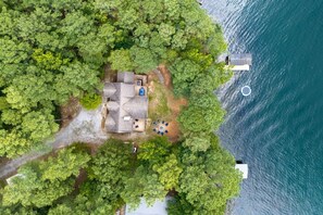 Vista aérea de una casa con patio, rodeada de árboles frondosos y una masa de agua.