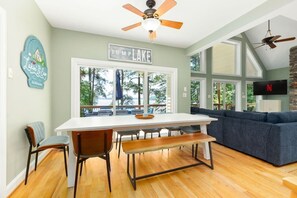 A dining area with a white table, wooden chairs, and a bench. There is a ceiling fan above the table. - Lakin` It Easy | Fire Pit+H20 Trampoline+GameRoom (Henrico)