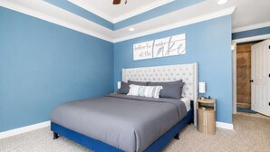A bedroom with a bed, a nightstand, a wall clock, and a door leading to another room.