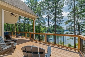 A covered deck with outdoor furniture, a view of a lake, and tall pine trees. - Lakin` It Easy | Fire Pit+H20 Trampoline+GameRoom (Henrico)