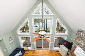 A room with a sloped ceiling, a ceiling fan, a view of the outdoors, a fireplace, and a television.