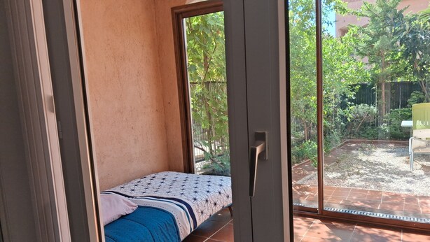 Ein Zimmer mit einem Bett, einer Schiebetür zu einem Gartenbereich mit einem Garten und einem Stuhl.