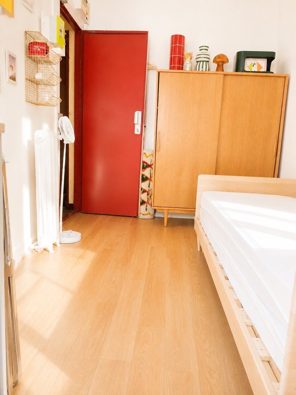 Een slaapkamer met een houten garderobe, een bed, een radiator en een deur.