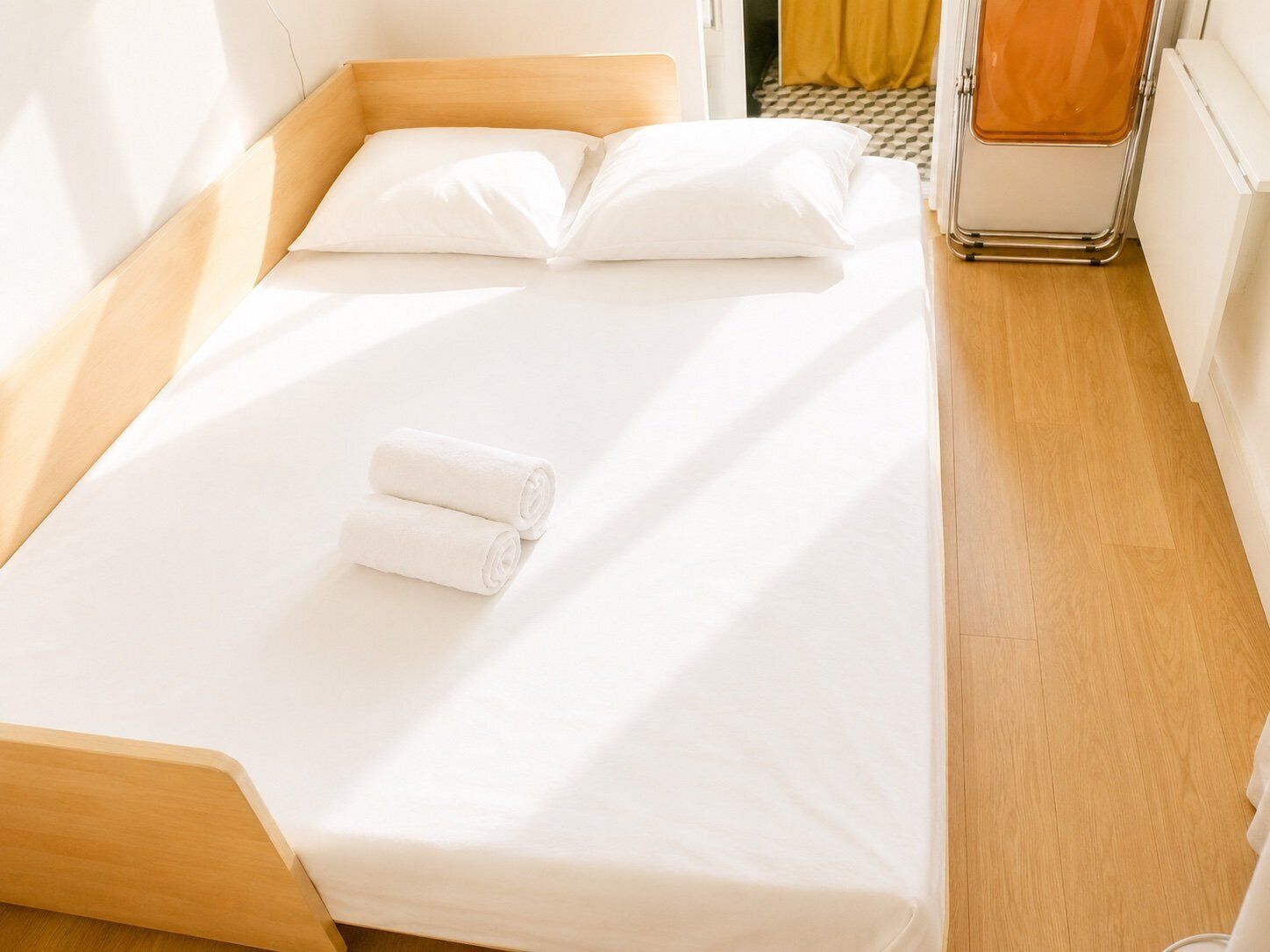 Un lit simple avec du linge de lit blanc, une tête de lit en bois et une serviette enroulée.