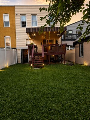 A residential backyard with a wooden deck, a small staircase, and a well-maintained lawn. - 2BR Apt • 9 Min to MetLife • 15 Min to NYC • (North Bergen)