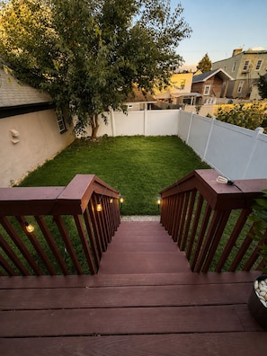 A wooden deck with a staircase leading to a grassy backyard. - 2BR Apt • 9 Min to MetLife • 15 Min to NYC • (North Bergen)
