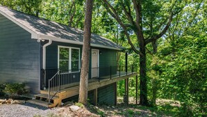 Eine kleine, eingeschossige Hütte mit Veranda und Terrasse, umgeben von dichtem Wald.
