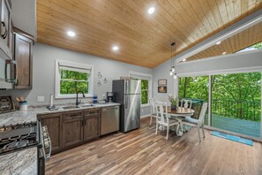 A modern kitchen with a central island, stainless steel appliances, and a dining area with a view of the outdoors. - Mountain Music Romantic Private Brow Cottage with Hot Tub (Fort Payne)