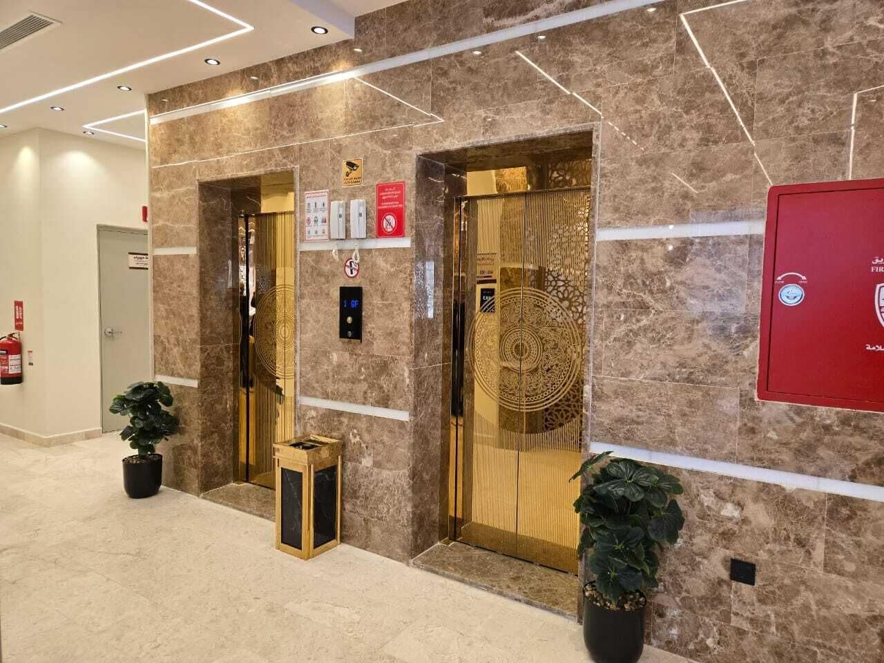 Un ascenseur doté d’une porte décorative dorée, d’une alarme incendie et d’une boîte rouge pour les situations d’urgence.