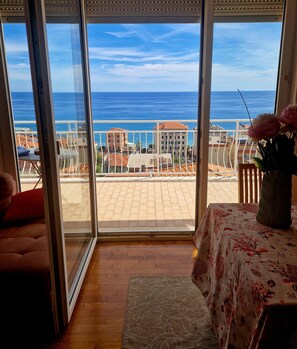 A room with a view of the sea through large glass doors, a wooden floor, a table with a floral tablecloth, and a chair. - detached villa in Varazze, sea view and private car parking space (Varazze)