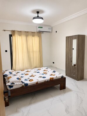 A bedroom with a bed, an air conditioning unit, a wardrobe, and a ceiling fan.