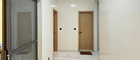 A hallway with a marble floor, a door with a metal frame, and a ceiling light.