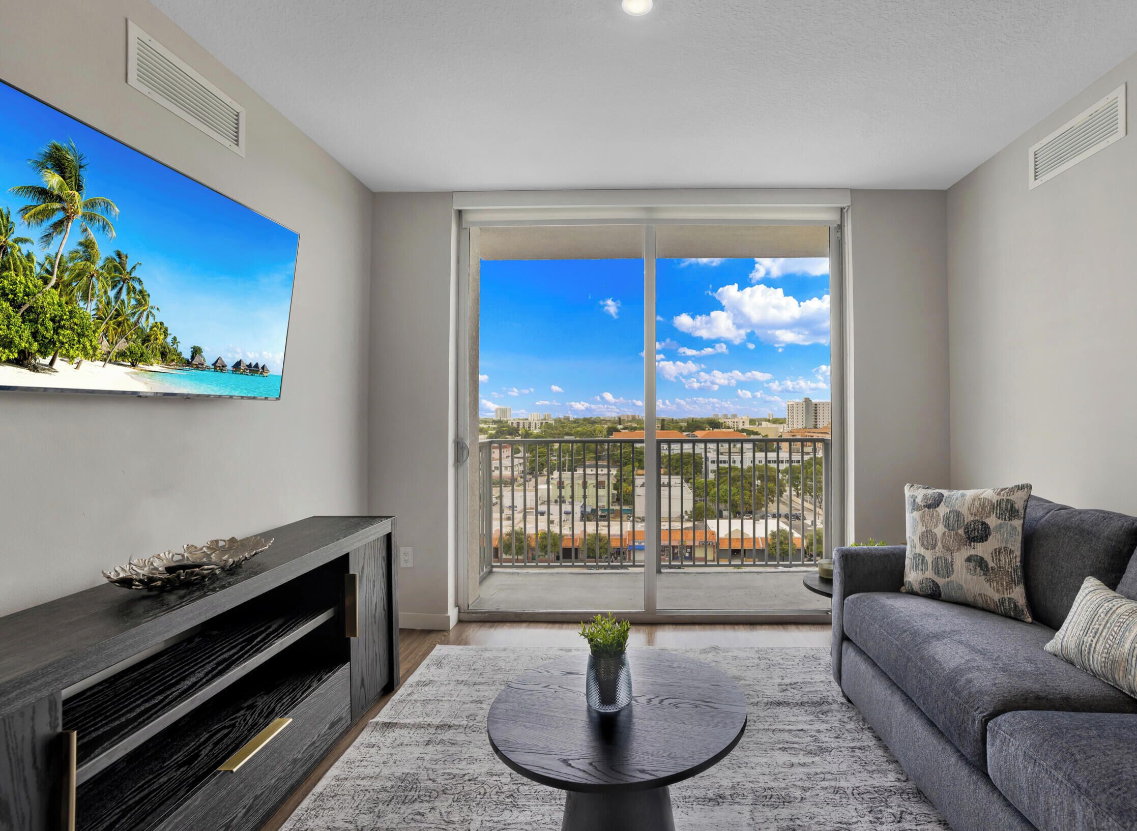 A modern living room with a large window, a flat-screen TV, a grey sofa, and a coffee table.