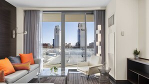 Ein modernes Hotelzimmer mit Glastrennwand, einer Couch, einem Sessel, einem Couchtisch und einem Fernseher.