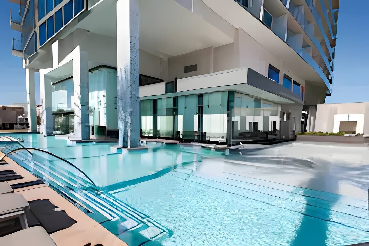 A modern hotel with a rooftop pool, large glass windows, and a clear sky.