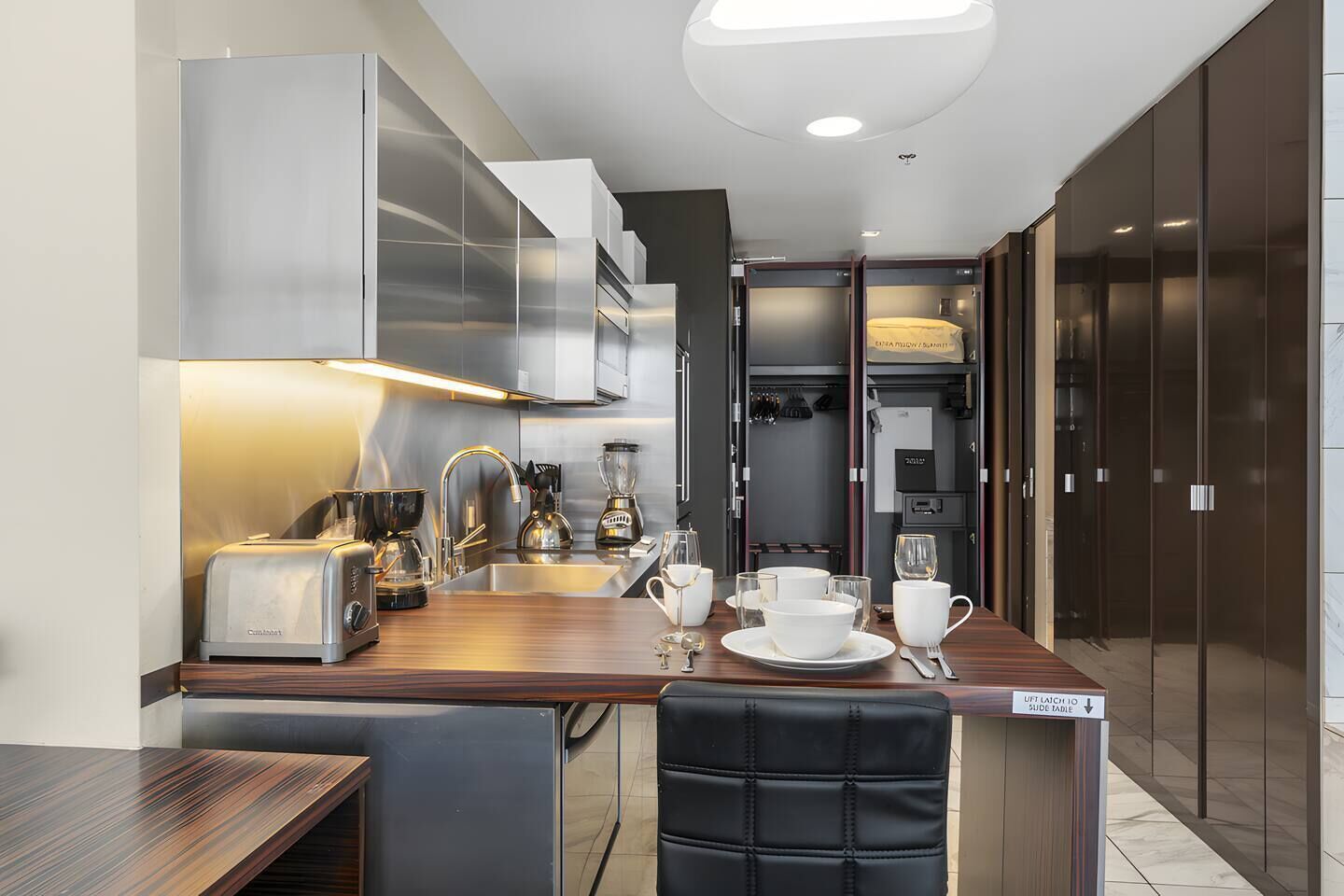 A compact kitchen with modern appliances, a dining area with a table set for two, and a wardrobe with sliding doors.