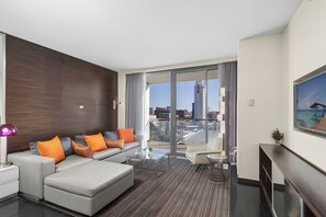 Una habitació d'hotel moderna amb un sofà, una taula de centre de vidre, una televisió de pantalla plana i vista a la ciutat.