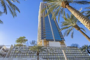 Un edifici alt amb façana de vidre moderna, palmeres i el text 'PALM BEACH' a la part inferior.
