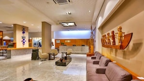 A hotel lobby with a reception desk, seating area, and a wall with wooden sculptures.