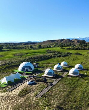 A series of dome-shaped structures in a grassy field with a mountainous backdrop. - Nomad Space (Bar-Bulak)