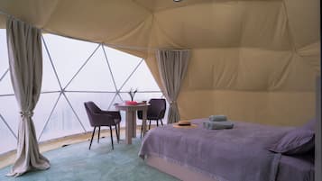 Una tenda-camera con un letto, due sedie, un tavolino e vista dalla finestra.